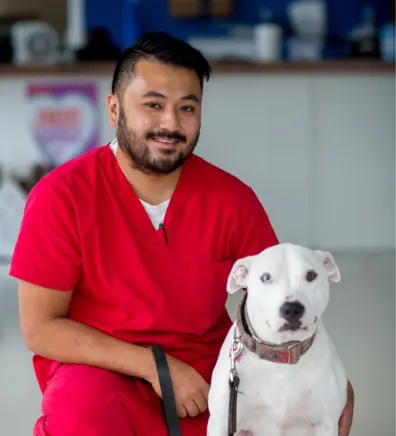 Arnold in red scrubs with a white dog from Tacoma Animal Hospital